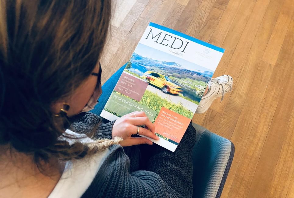 Eine Patientin blättert im Wartezimmer durch ein Kundenmagazin mit Fotoreportagen